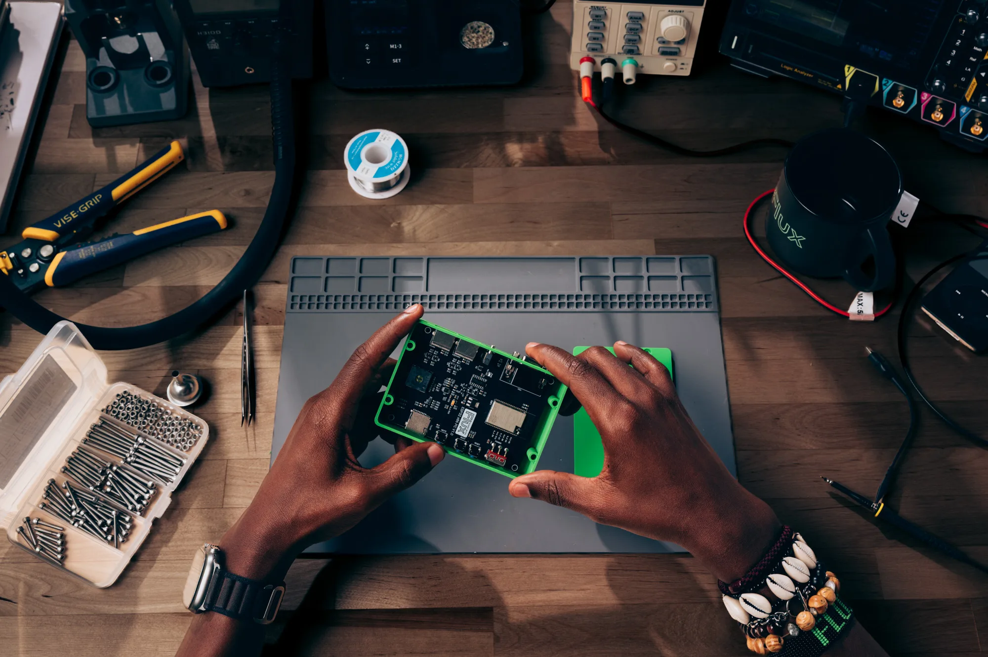 An engineer holding a circuit board in its enclosure above an electronics workbench